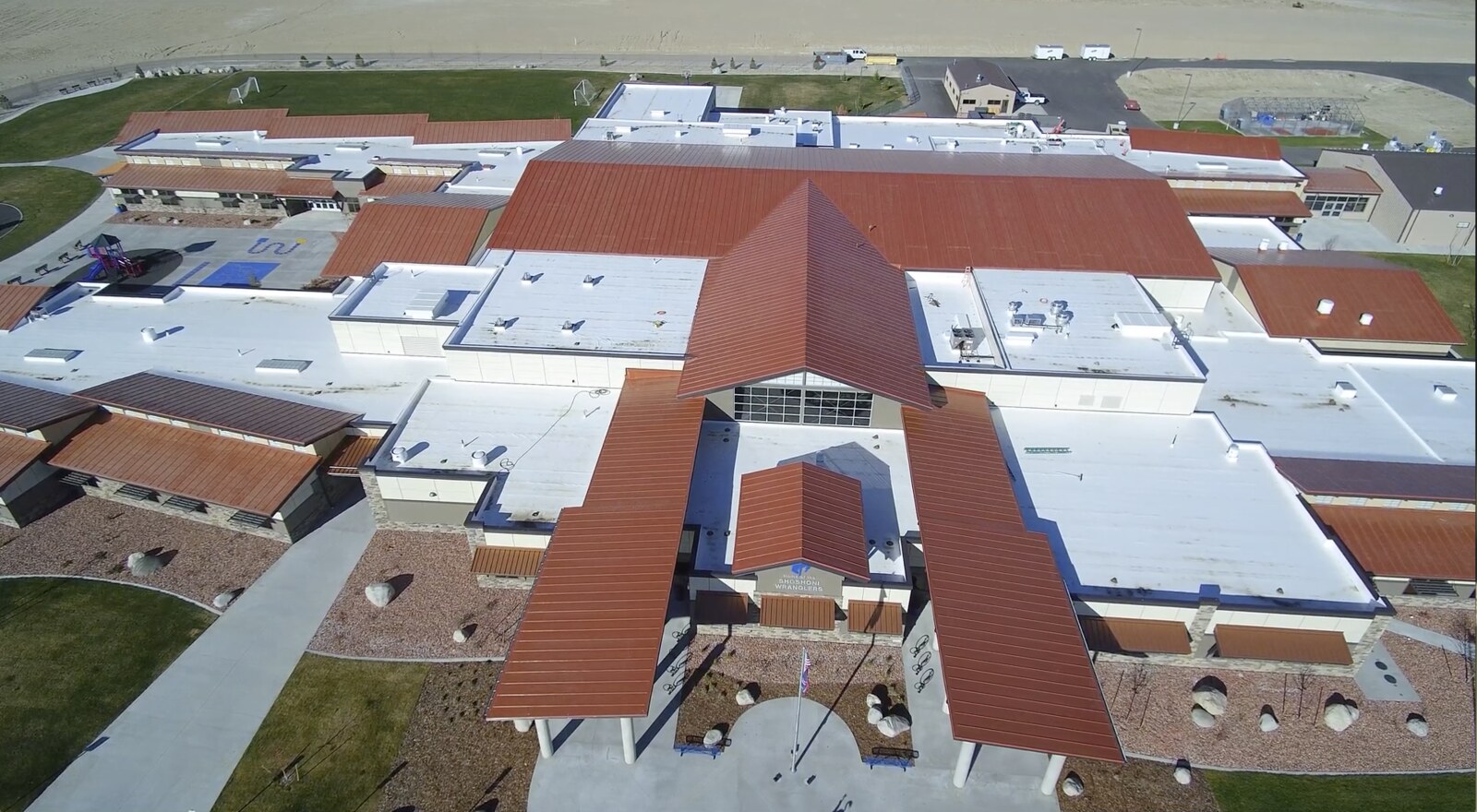Aerial view of a Lowe Roofing project with red pitched roofs and broad white low-slope roof areas