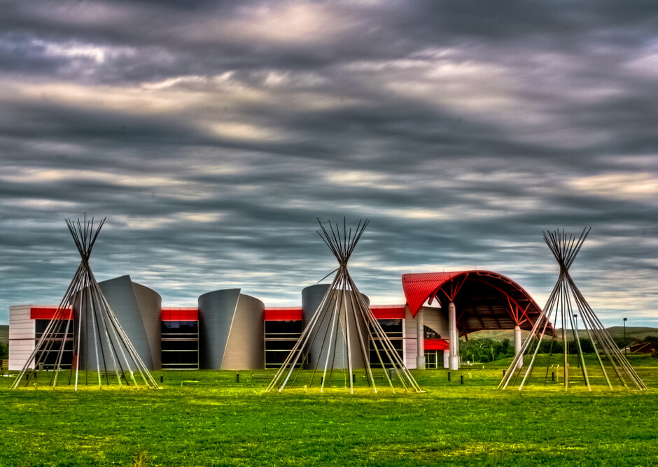 Building with a curved red roof and wooden teepee forms on the surrounding lawn